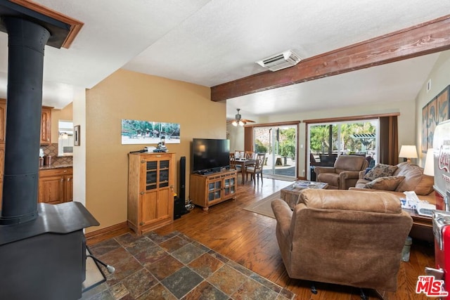 living room with beamed ceiling, dark hardwood / wood-style floors, a wood stove, and ceiling fan