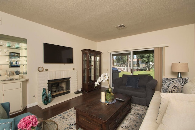 living room with sink, a textured ceiling, a brick fireplace, and hardwood / wood-style flooring