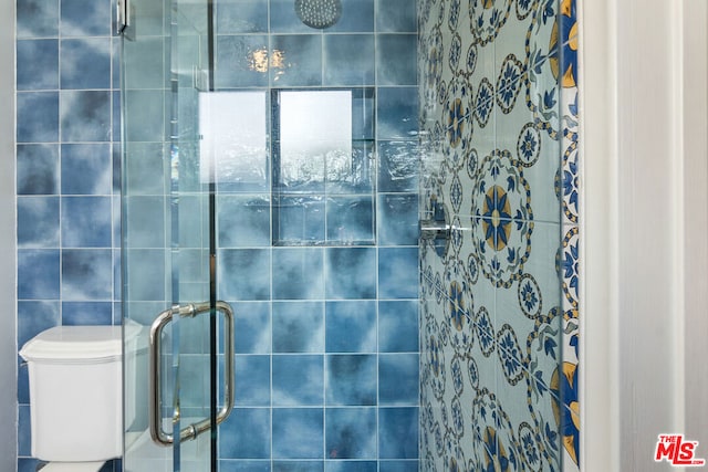 bathroom with toilet, an enclosed shower, and tile walls