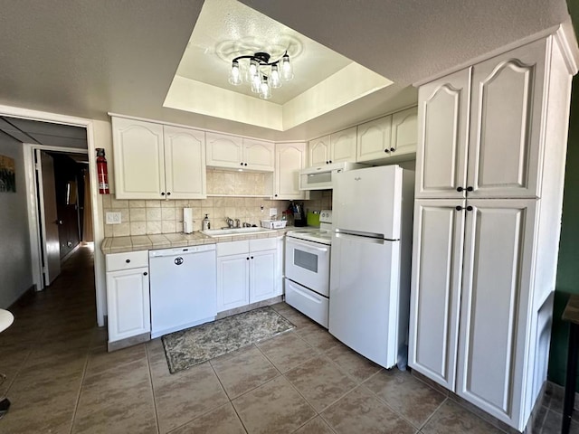 kitchen with dark tile patterned flooring, sink, a tray ceiling, white appliances, and white cabinetry