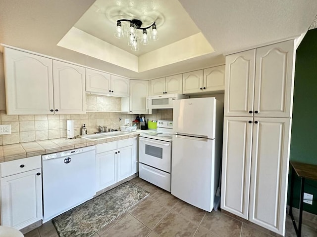 kitchen with white cabinetry, sink, a tray ceiling, and white appliances