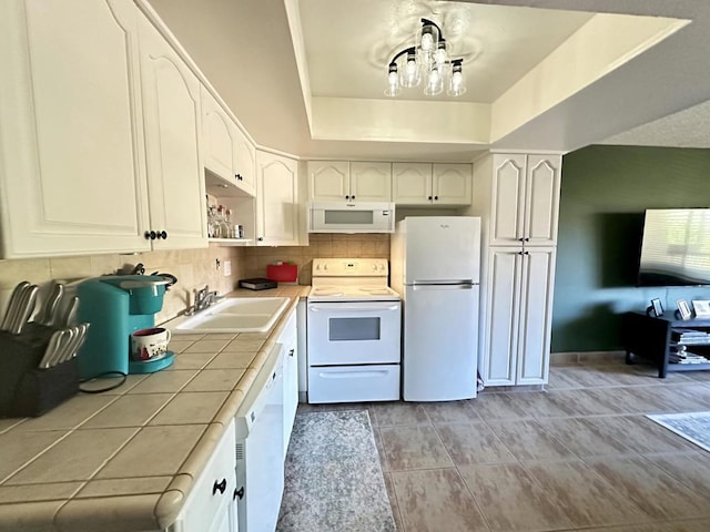 kitchen featuring white appliances, tile counters, white cabinetry, sink, and a tray ceiling