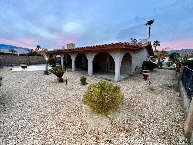 back house at dusk featuring a mountain view and a patio area