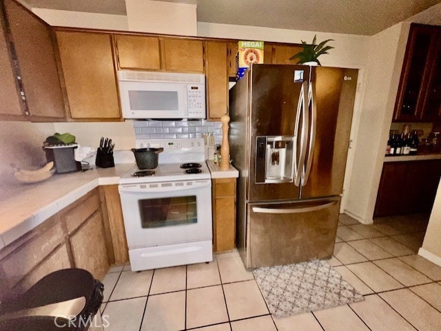 kitchen with light tile patterned floors, white appliances, and backsplash