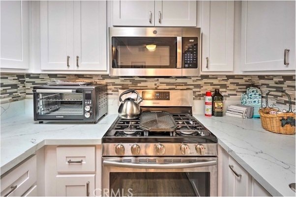 kitchen featuring light stone countertops, decorative backsplash, appliances with stainless steel finishes, and white cabinetry