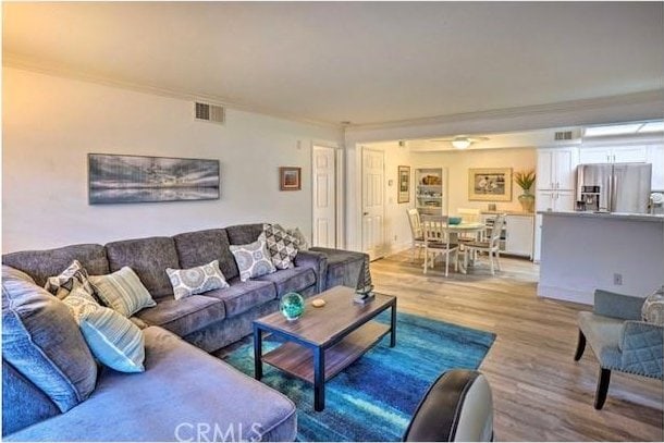 living room with crown molding, visible vents, and light wood-style floors