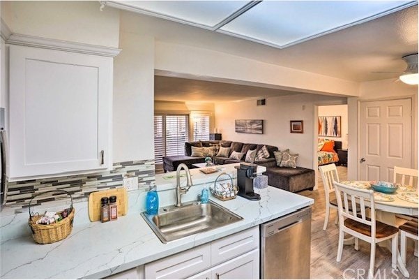 kitchen with tasteful backsplash, sink, dishwasher, white cabinetry, and light hardwood / wood-style flooring