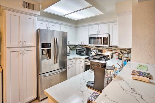 kitchen featuring decorative backsplash, appliances with stainless steel finishes, light stone counters, and white cabinetry