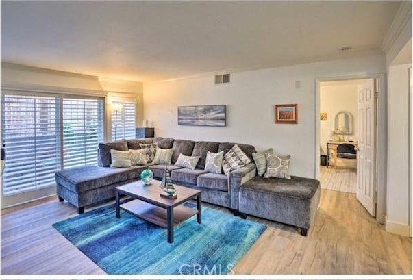 living area with wood finished floors, visible vents, and crown molding