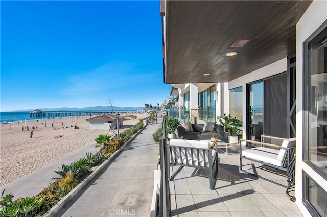 balcony featuring a water view, a view of the beach, and an outdoor living space