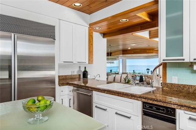 kitchen featuring sink, wood ceiling, white cabinetry, stainless steel appliances, and dark stone counters