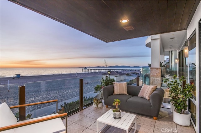 balcony at dusk featuring a view of the beach and a water view