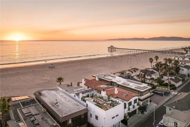 aerial view at dusk featuring a water view and a view of the beach