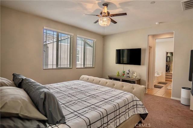 bedroom with ensuite bathroom, light colored carpet, and ceiling fan