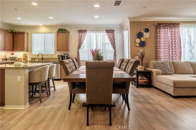 dining area featuring a wealth of natural light, sink, crown molding, and light hardwood / wood-style floors