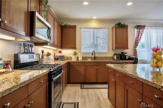 kitchen with stainless steel appliances, light wood finished floors, a sink, light stone counters, and ornamental molding