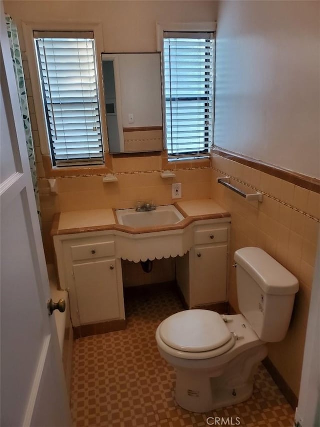 bathroom with toilet, tile walls, a healthy amount of sunlight, and sink