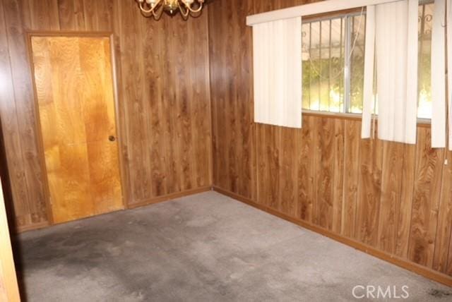 spare room with carpet floors, a notable chandelier, and wood walls