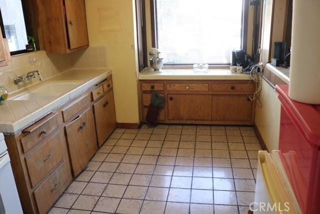 kitchen featuring tasteful backsplash, tile counters, light tile patterned flooring, and sink