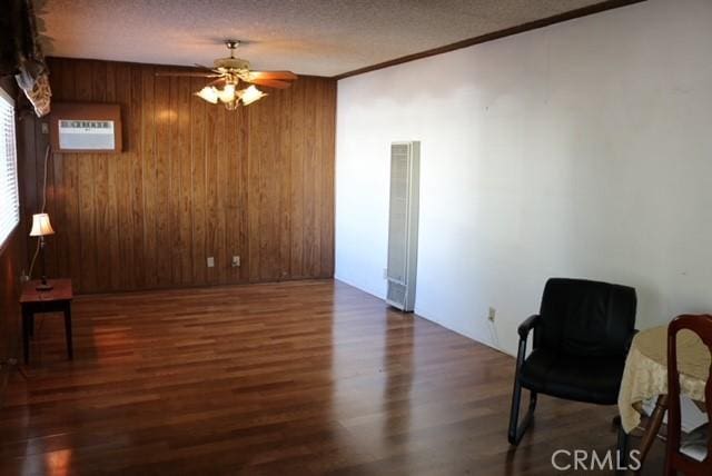 sitting room with dark hardwood / wood-style flooring, an AC wall unit, ceiling fan, and wood walls