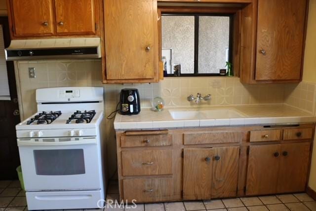 kitchen featuring tile countertops, sink, range hood, and white gas range oven