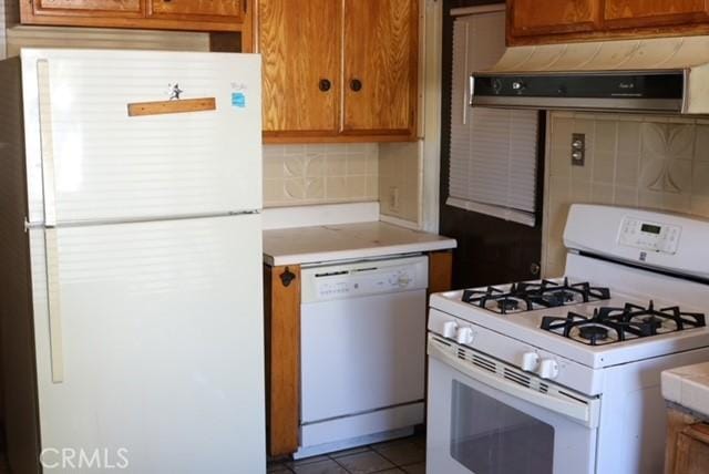 kitchen featuring decorative backsplash, tile patterned flooring, extractor fan, and white appliances