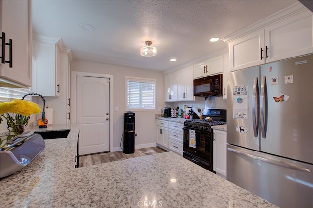 kitchen with white cabinetry, light stone countertops, black appliances, and light hardwood / wood-style flooring