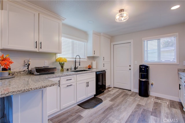 kitchen featuring black dishwasher, white cabinetry, light stone countertops, light hardwood / wood-style floors, and sink