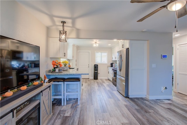 kitchen with a breakfast bar, white cabinetry, light wood-type flooring, pendant lighting, and light stone counters