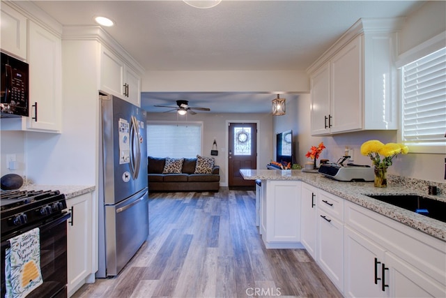 kitchen with light stone counters, black appliances, light wood-type flooring, and white cabinets