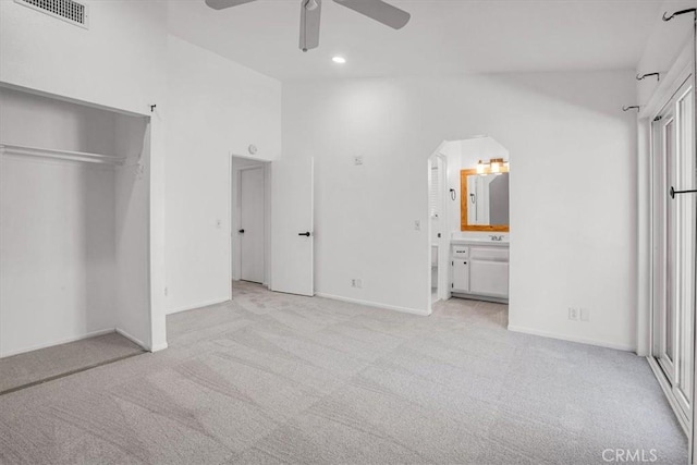 unfurnished bedroom featuring light carpet, ensuite bathroom, ceiling fan, high vaulted ceiling, and a closet