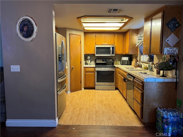 kitchen with tile countertops, stainless steel appliances, sink, and light wood-type flooring