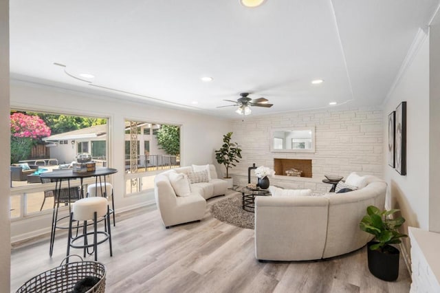 living room with ornamental molding, ceiling fan, a fireplace, and light hardwood / wood-style flooring