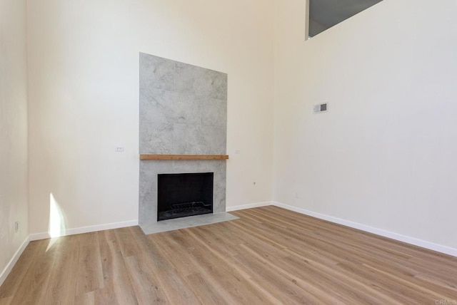 unfurnished living room featuring light hardwood / wood-style flooring, a tiled fireplace, and a high ceiling