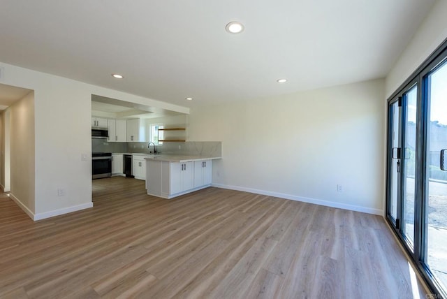 kitchen with kitchen peninsula, white cabinets, sink, light hardwood / wood-style floors, and stainless steel appliances