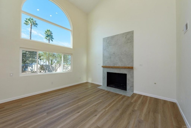 unfurnished living room with a high ceiling, wood-type flooring, and a tile fireplace