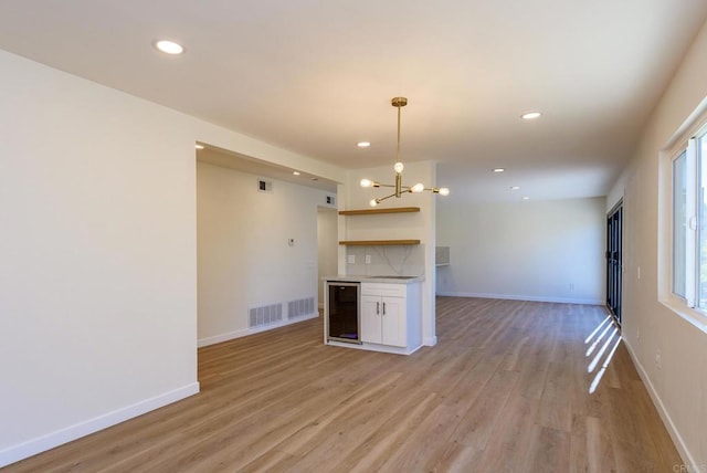 kitchen with white cabinetry, light hardwood / wood-style floors, pendant lighting, beverage cooler, and a notable chandelier