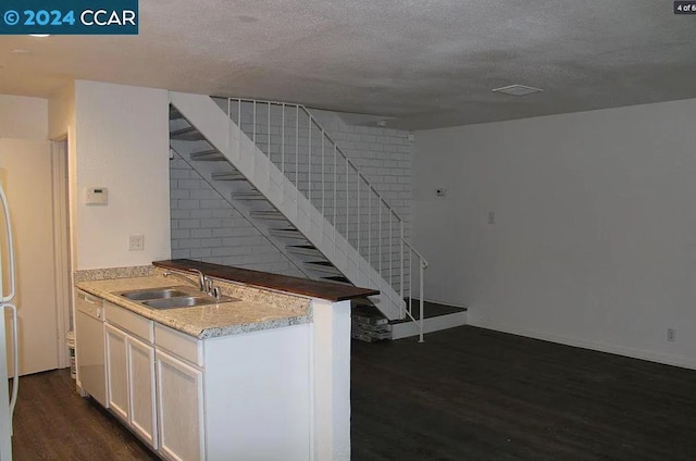 kitchen with sink, dark wood-type flooring, kitchen peninsula, and a textured ceiling