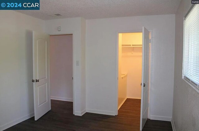 unfurnished bedroom with dark wood-type flooring, multiple windows, a walk in closet, and a closet