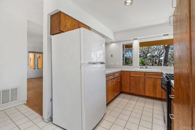 kitchen with black range with gas stovetop, light tile patterned floors, sink, and white refrigerator