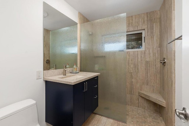 bathroom with toilet, tiled shower, and vanity