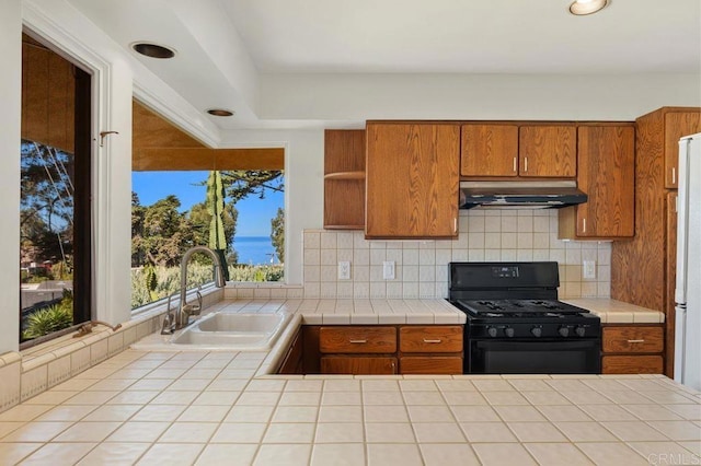 kitchen with tasteful backsplash, tile countertops, white fridge, black range with gas stovetop, and sink