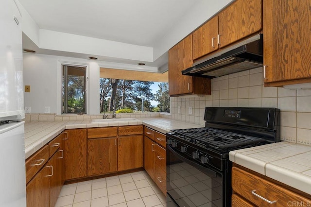 kitchen featuring tile counters, white refrigerator, tasteful backsplash, black gas stove, and light tile patterned flooring