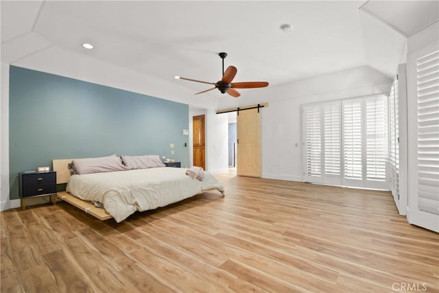 bedroom featuring a barn door, ceiling fan, and light wood-type flooring