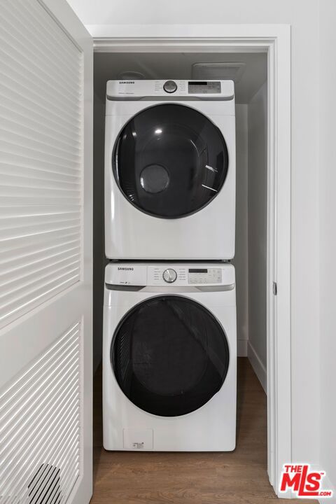 clothes washing area with hardwood / wood-style floors and stacked washer / drying machine