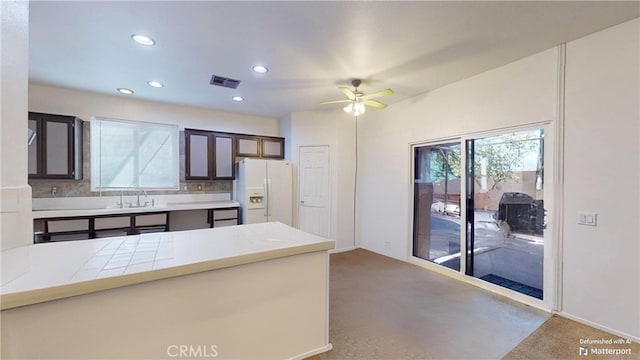 kitchen with ceiling fan, white fridge with ice dispenser, kitchen peninsula, decorative backsplash, and dark brown cabinets