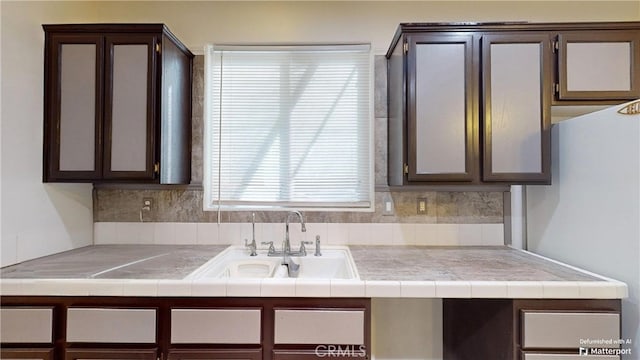 kitchen featuring tile countertops, dark brown cabinets, decorative backsplash, and sink