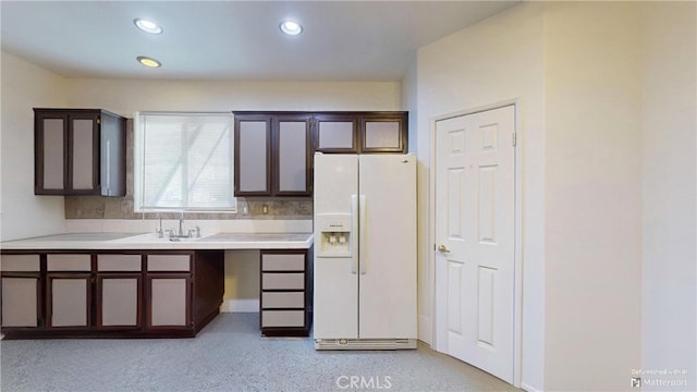 kitchen featuring dark brown cabinets, sink, white fridge with ice dispenser, and backsplash