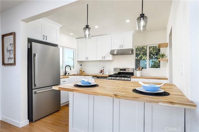 kitchen featuring wood counters, white cabinets, hanging light fixtures, and appliances with stainless steel finishes