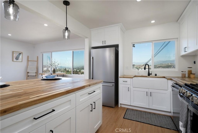 kitchen with pendant lighting, a sink, appliances with stainless steel finishes, light wood finished floors, and wooden counters